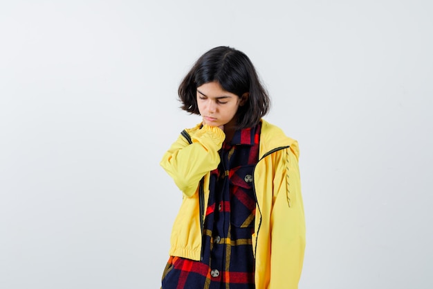Młoda dziewczyna kładzie rękę na szyi w kraciaste koszule i żółtą kurtkę i wygląda na zmęczoną. przedni widok.