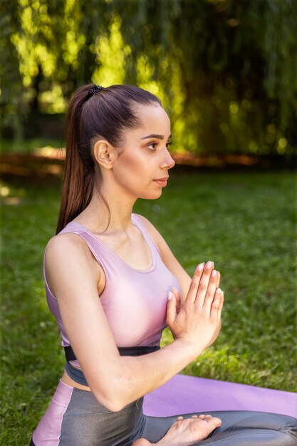 Młoda dziewczyna medytuje rękami na piersi w pozycji lotosu w parku