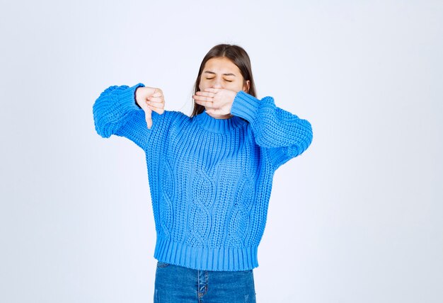 młoda dziewczyna model w niebieskim swetrze, ziewanie i pokazując kciuk w dół.