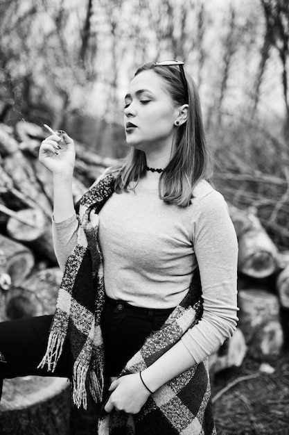 Bezpłatne zdjęcie młoda dziewczyna pali papierosy na zewnątrz tło drewniane kikuty koncepcja uzależnienia od nikotyny przez nastolatków