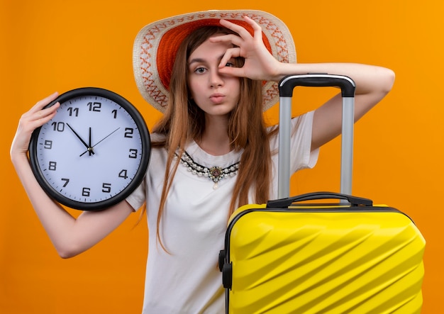 Bezpłatne zdjęcie młoda dziewczyna podróżnika na sobie kapeluszową walizkę na odosobnionej pomarańczowej ścianie