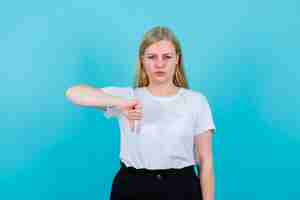 Bezpłatne zdjęcie młoda dziewczyna pokazuje gest niechęci kciukiem na niebieskim tle