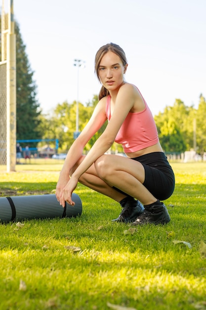 Młoda dziewczyna siedzi obok na macie sportowej i patrzy w kamerę