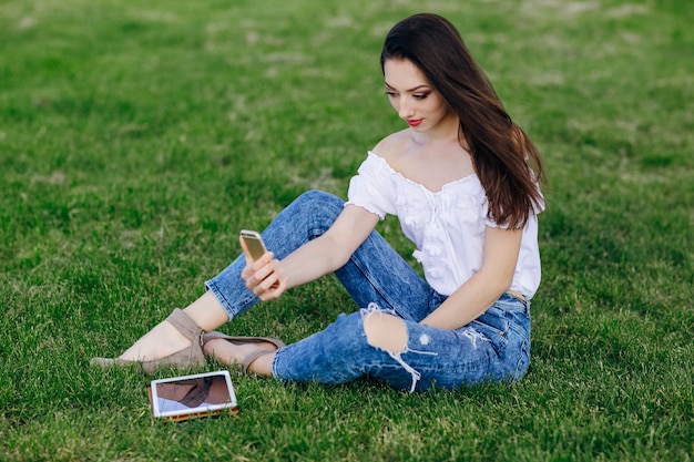 Młoda dziewczyna siedzi w parku robienia zdjęcia
