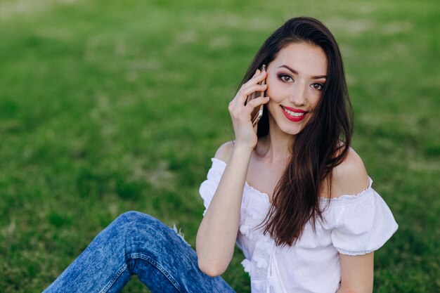 Młoda dziewczyna siedzi w parku rozmawia smartphone podczas uśmiecha
