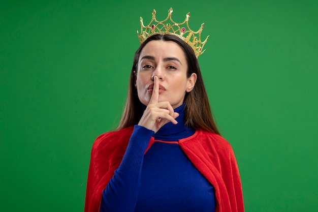 Bezpłatne zdjęcie młoda dziewczyna superbohatera nosząc koronę pokazując gest ciszy na białym tle na zielono