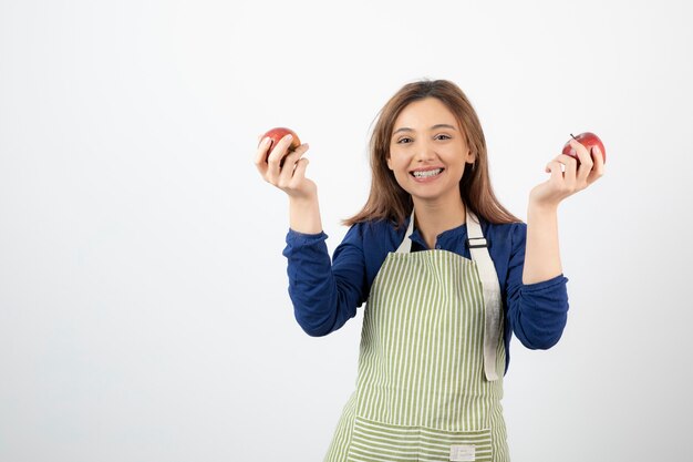 młoda dziewczyna trzyma czerwone jabłka, uśmiechając się na białym tle.