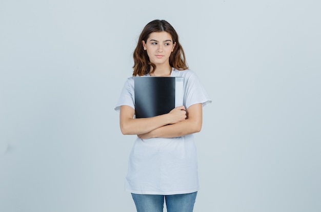 Młoda dziewczyna trzyma folder w białej koszulce i wygląda zamyślony. przedni widok.