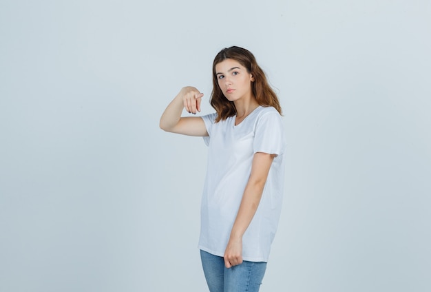 Młoda dziewczyna w białej koszulce, wskazując na aparat i patrząc rozsądnie, widok z przodu.