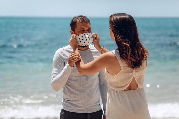 Młoda dziewczyna w białej sukni ostrożnie zakłada na męża ochronną maskę medyczną z czarną polką, aby uchronić go przed wirusem. koncepcja rodziny