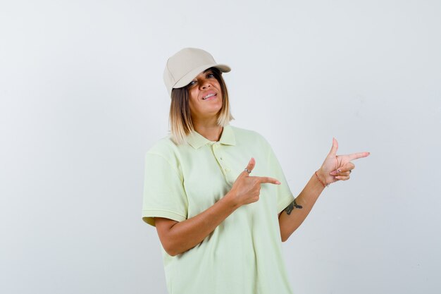 Młoda dziewczyna w t-shirt i czapkę wskazującą w prawo z palcami wskazującymi i ładny widok z przodu.