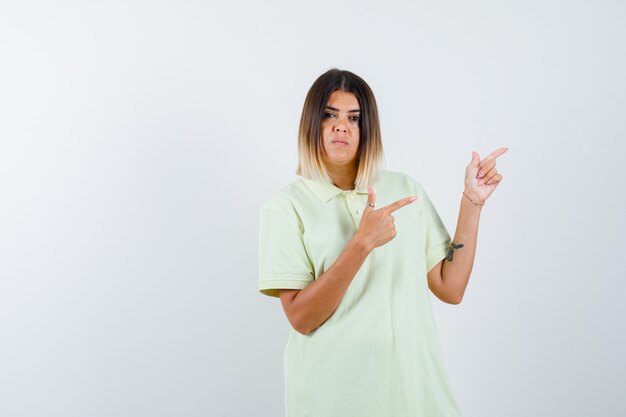 Młoda dziewczyna w t-shirt, wskazując w prawo z palcami wskazującymi i patrząc poważny, przedni widok.