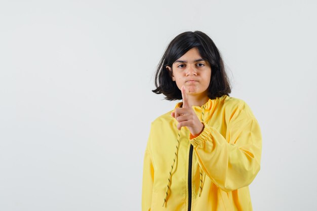 Młoda dziewczyna, wskazując palcem wskazującym na aparat w żółtej bomber Jacket i patrząc poważnie