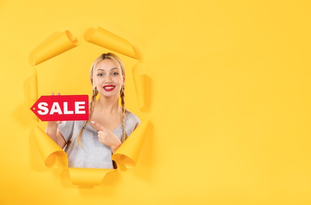 Bezpłatne zdjęcie młoda dziewczyna z napisem sprzedaży na rozdartym żółtym tle zakupy twarzy