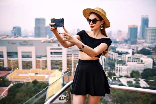 Młoda elegancka kobieta ubrana w modny letni strój co turystyczne selfie na tarasie luksusowego hotelu