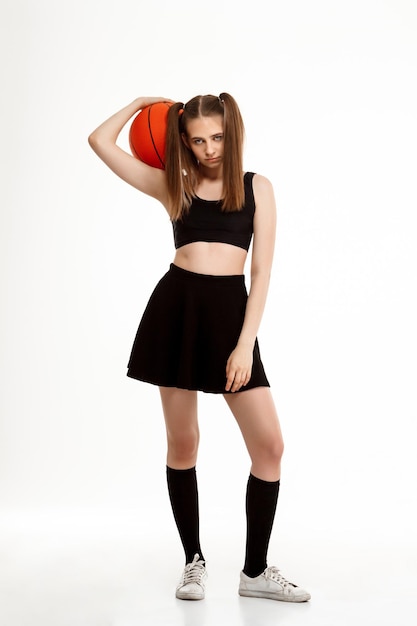 Młoda emocjonalna ładna dziewczyna pozuje do koszykówki na białym tle