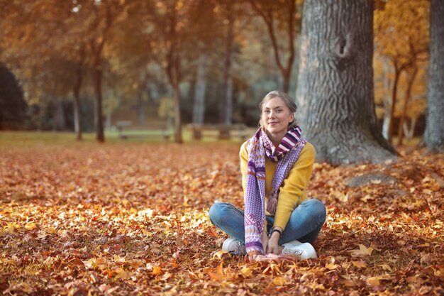 Młoda europejska kobieta siedzi na ziemi w jesiennym parku