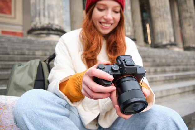 Młoda fotografka studencka siedzi na schodach ulicznych i sprawdza swoje zdjęcia na profesjonalnym aparacie