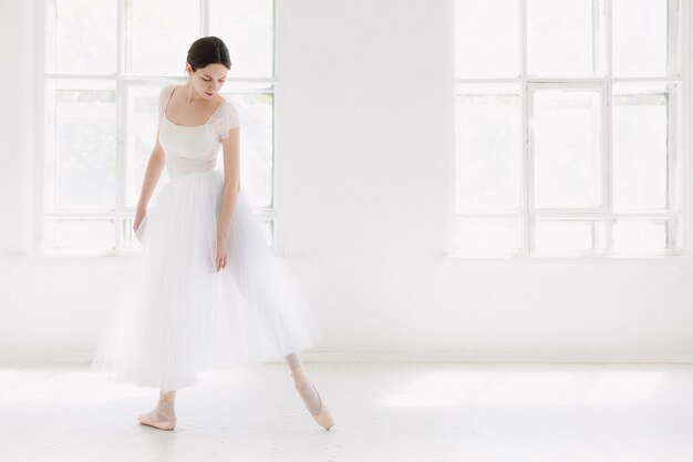 Młoda i niezwykle piękna baletnica pozuje i tańczy w białym studio