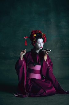 Młoda japonka jako gejsza na ciemnozielonym. styl retro, porównanie koncepcji epok.