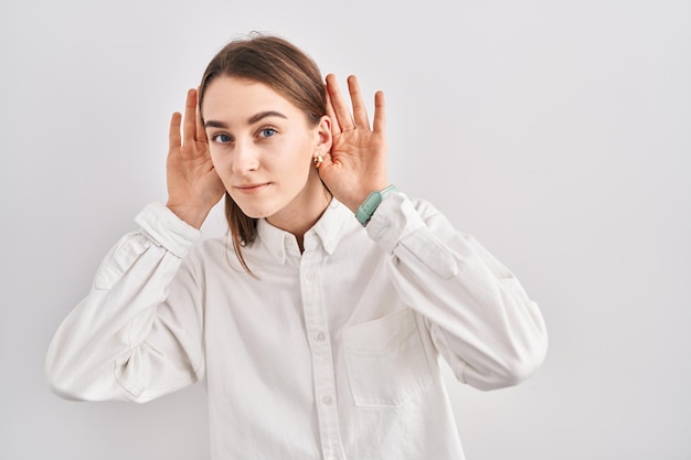 Młoda kaukaska kobieta stojąca nad odizolowanym tłem, próbująca usłyszeć obie ręce na geście ucha, ciekawa plotek, głuchoniemych problemów ze słuchem