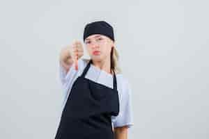 Bezpłatne zdjęcie młoda kelnerka pokazuje kciuk w dół w widoku z przodu mundurze i fartuchu.