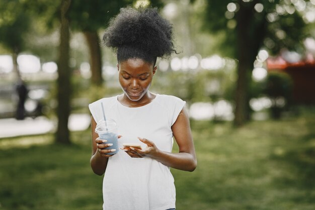 Młoda kobieta afro-amerykańska patrząca na telefon w parku