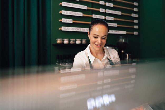 Młoda kobieta baristka stojąca wewnątrz lady z kawą