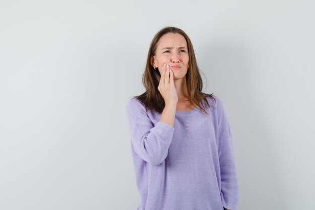 Młoda kobieta cierpiąca na ból zęba w liliowej bluzce i wyglądająca na zmartwioną. przedni widok.