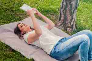 Bezpłatne zdjęcie młoda kobieta czyta książkę w parku leżącej na trawie. selektywne fokus. m? oda mi? a uprzejma kobieta le? y na zielonej trawie i czyta ksi ?? ki przeciwko city park.