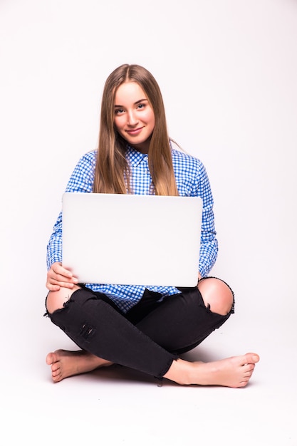 Młoda kobieta dorywczo siedzi uśmiechnięty trzymając laptop na białym tle na białej ścianie
