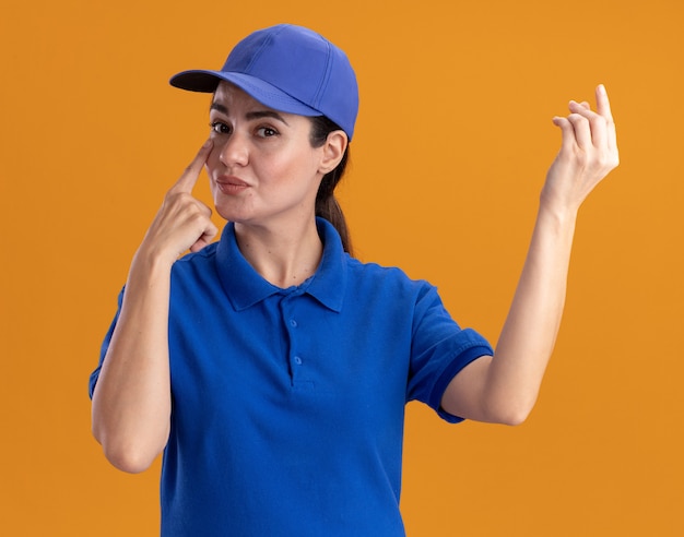 Młoda kobieta dostawy w mundurze i czapce robi gest pieniędzy kładąc palec pod oko