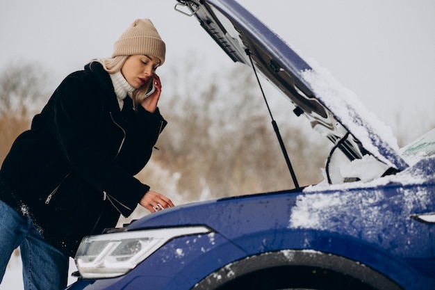 Młoda kobieta dzwoni do telefonu po awarii jej samochodu w sezonie zimowym