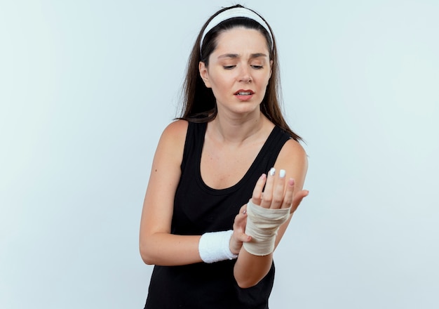 młoda kobieta fitness w opasce patrząc na jej zabandażowany nadgarstek uczucie bólu stojącego nad białą ścianą