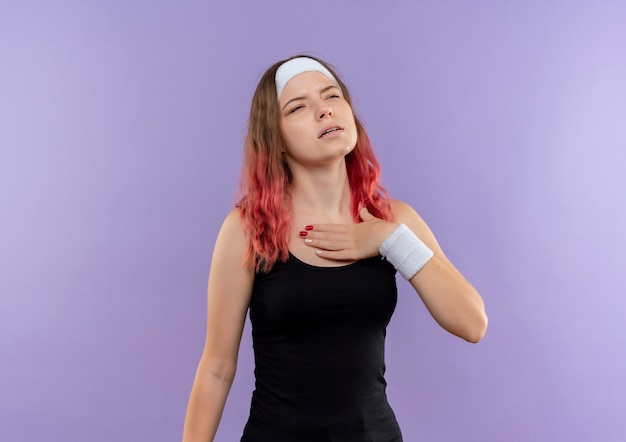 Młoda kobieta fitness w sportowej, trzymając rękę na jej klatce piersiowej, patrząc zmęczony stojący nad fioletową ścianą
