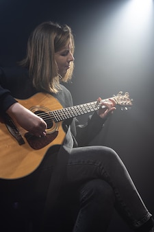 Młoda kobieta gra na gitarze akustycznej w ciemnym pokoju z zamgleniem