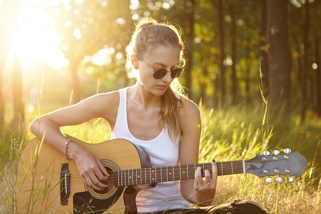 Młoda kobieta gra na gitarze w przyrodzie podczas zachodu słońca