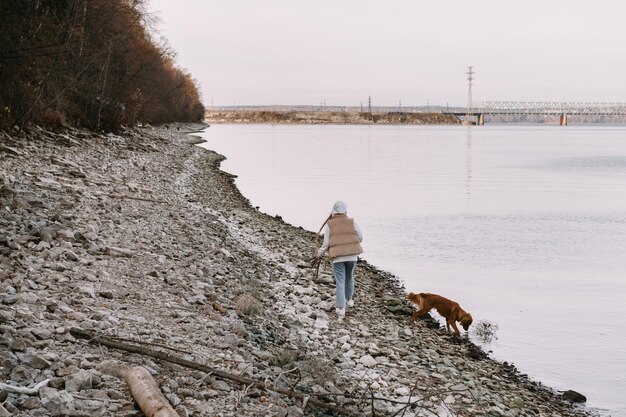 Młoda kobieta i pies retriever spacerują po brzegu rzeki w sezonie jesiennym