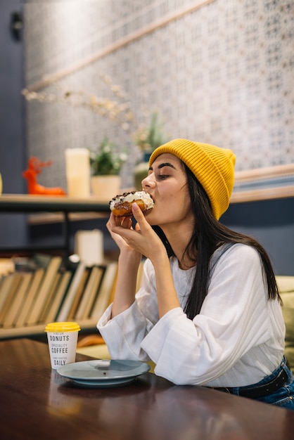 Bezpłatne zdjęcie młoda kobieta je deserowej pobliskiej filiżanki napój przy stołem