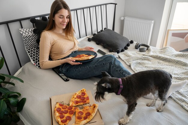 Młoda kobieta je pizzę na łóżku