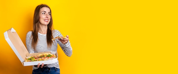 Młoda kobieta jedzenie świeżej gorącej pizzy z opakowania na żółtym tle. transparent.