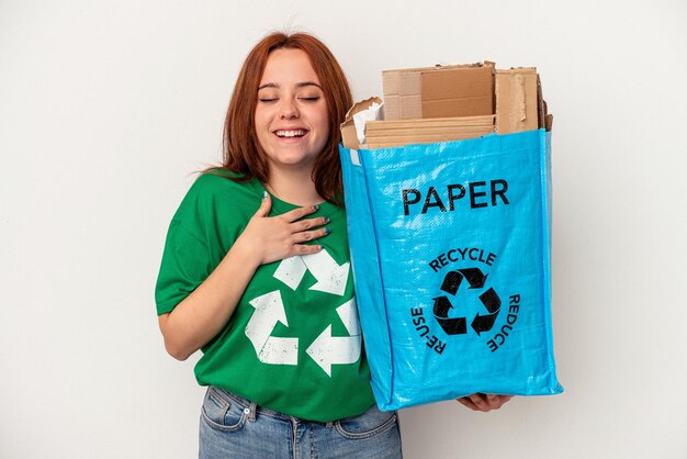 Młoda kobieta kaukaski z recyklingu papieru na białym tle śmieje się głośno trzymając rękę na klatce piersiowej.