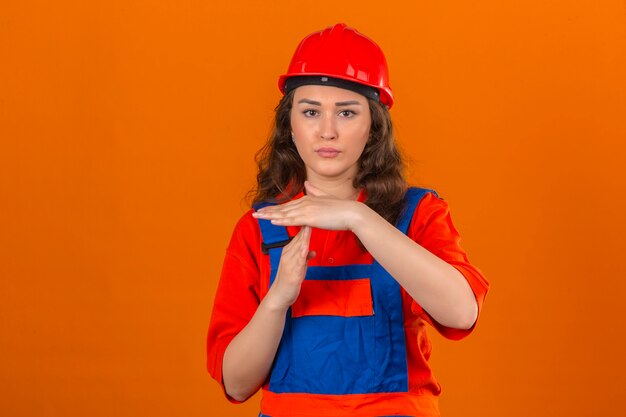 Młoda kobieta konstruktora w mundurze budowy i hełmie ochronnym patrząc przepracowany, czyniąc gest czasu na pojedyncze pomarańczowe ściany