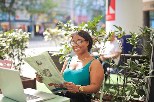 młoda kobieta korzysta z komputera i gazety w kawiarni na świeżym powietrzu