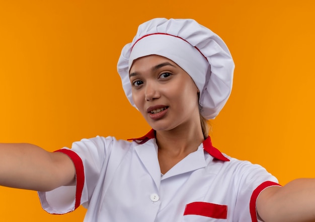 Bezpłatne zdjęcie młoda kobieta kucharz na sobie mundur szefa kuchni trzymając na pojedyncze pomarańczowe ściany