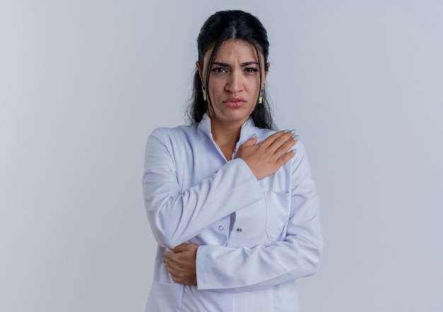 Młoda kobieta lekarz noszenie szaty medycznej patrząc kładąc rękę na barku cierpiących na ból na białym tle