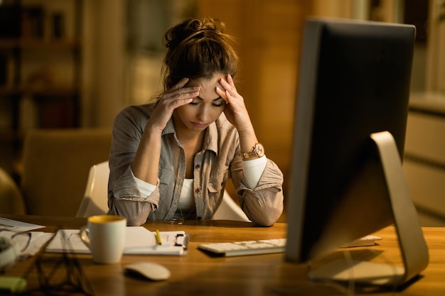 Młoda kobieta ma ból głowy po pracy na komputerze w nocy w domu