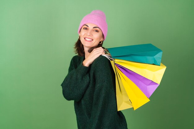 Młoda kobieta na zielono w ciepłym przytulnym swetrze i różowym kapeluszu z kolorowymi torbami na zakupy