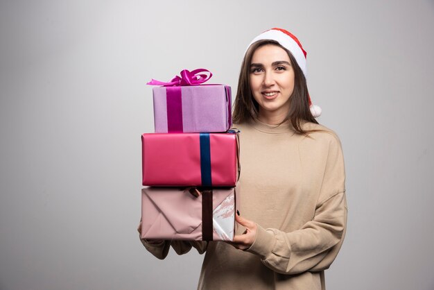 Młoda kobieta niosąca trzy pudełka prezentów świątecznych.