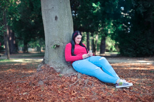 młoda kobieta oparta o drzewo używa smartfona